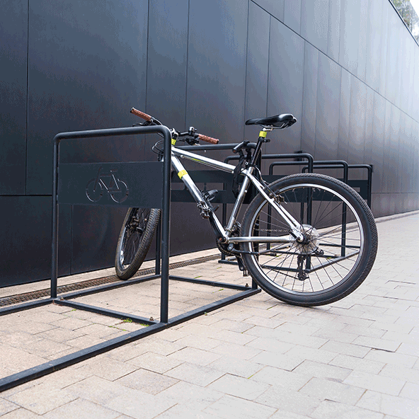 Na chodniku stoi stoja na rowery i przypięty do niego jeden rower.