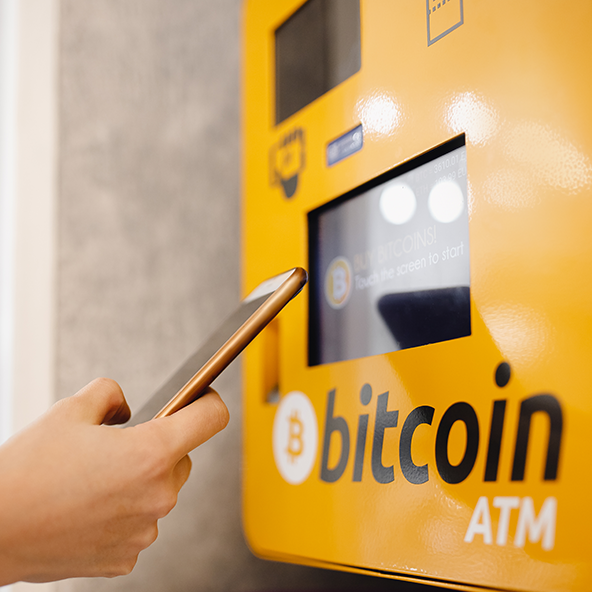 Dłoń trzyma w ręku telefon, obok jest żółty bitomat