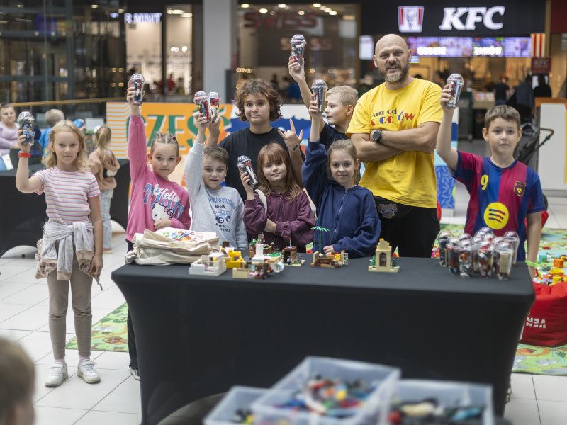 Dzieci i dorośli przy stole z pojemnikami klocków podczas warsztatów LEGO w Galerii Veneda.